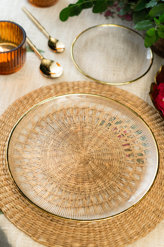 Woven placemat with gold rim on a table setting with glasses and cutlery.