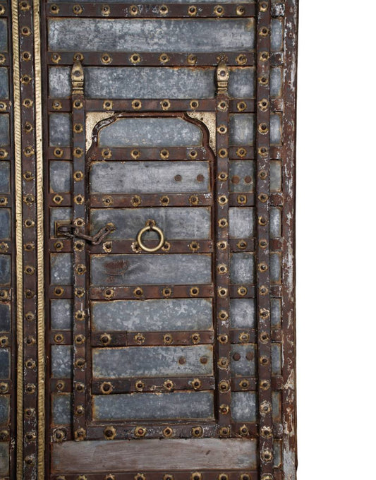 A close-up of an ornate traditional wooden door featuring weathered gray wood planks, dark brown metal crossbars, and numerous brass-colored rivets and decorative accents.