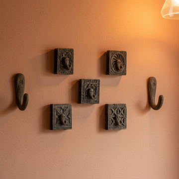 Five small dark carved wooden blocks with embossed floral and geometric designs, arranged on a plain light beige wall.