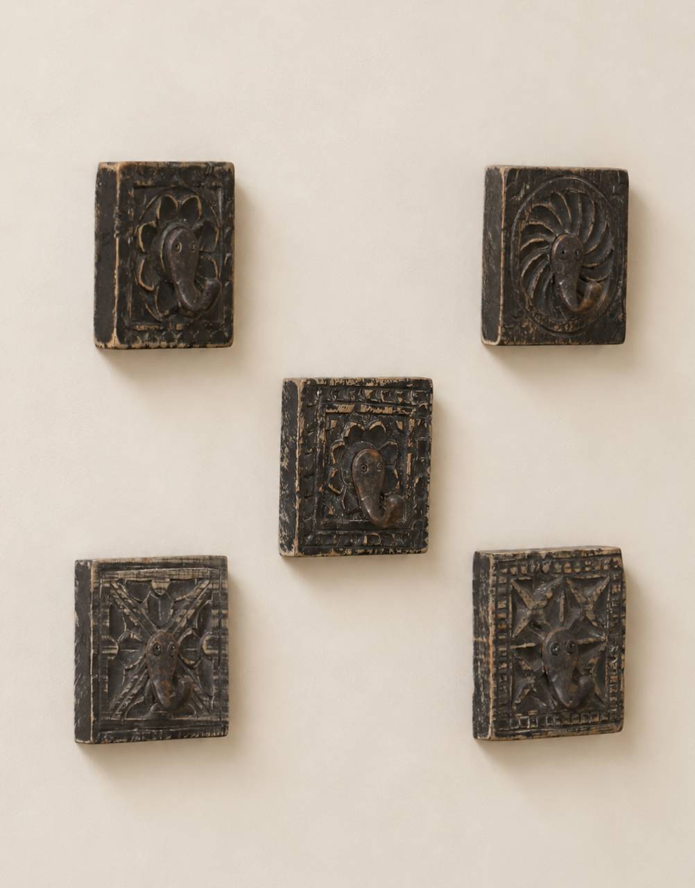 Five small dark carved wooden blocks with embossed floral and geometric designs, arranged on a plain light beige wall.