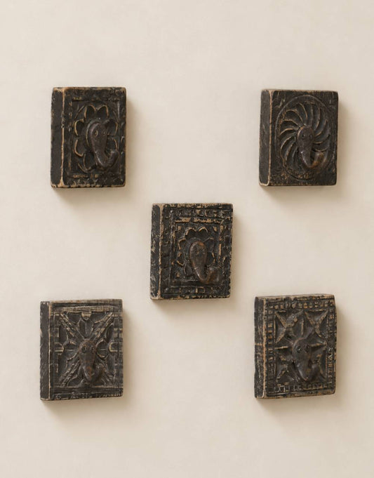 Five small dark carved wooden blocks with embossed floral and geometric designs, arranged on a plain light beige wall.