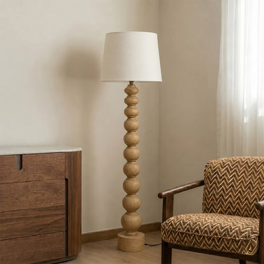 Wooden floor lamp with a white shade in a room with a wooden cabinet and patterned chair.