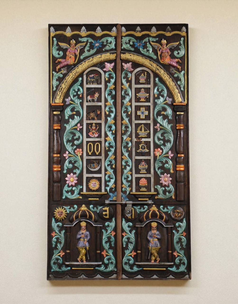 The panel features two guardian figures at the base, believed to be protectors of sacred thresholds, flanked by blooming floral motifs and flowing vines.