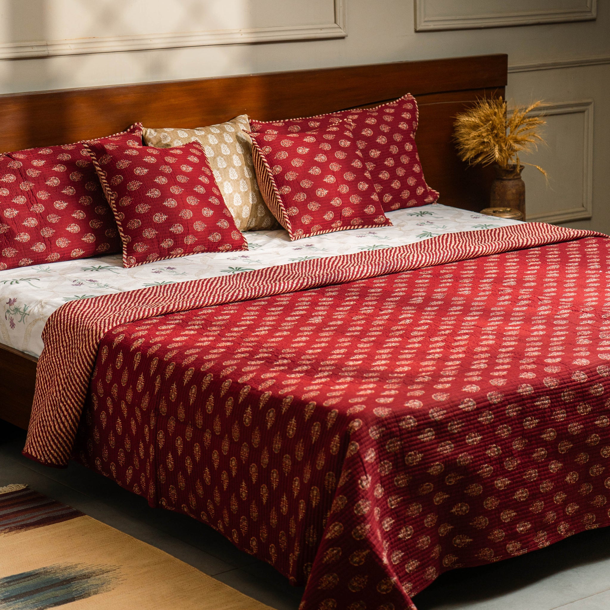 Bedroom with a bed covered in red and white patterned bedding, pillows, and a rug.