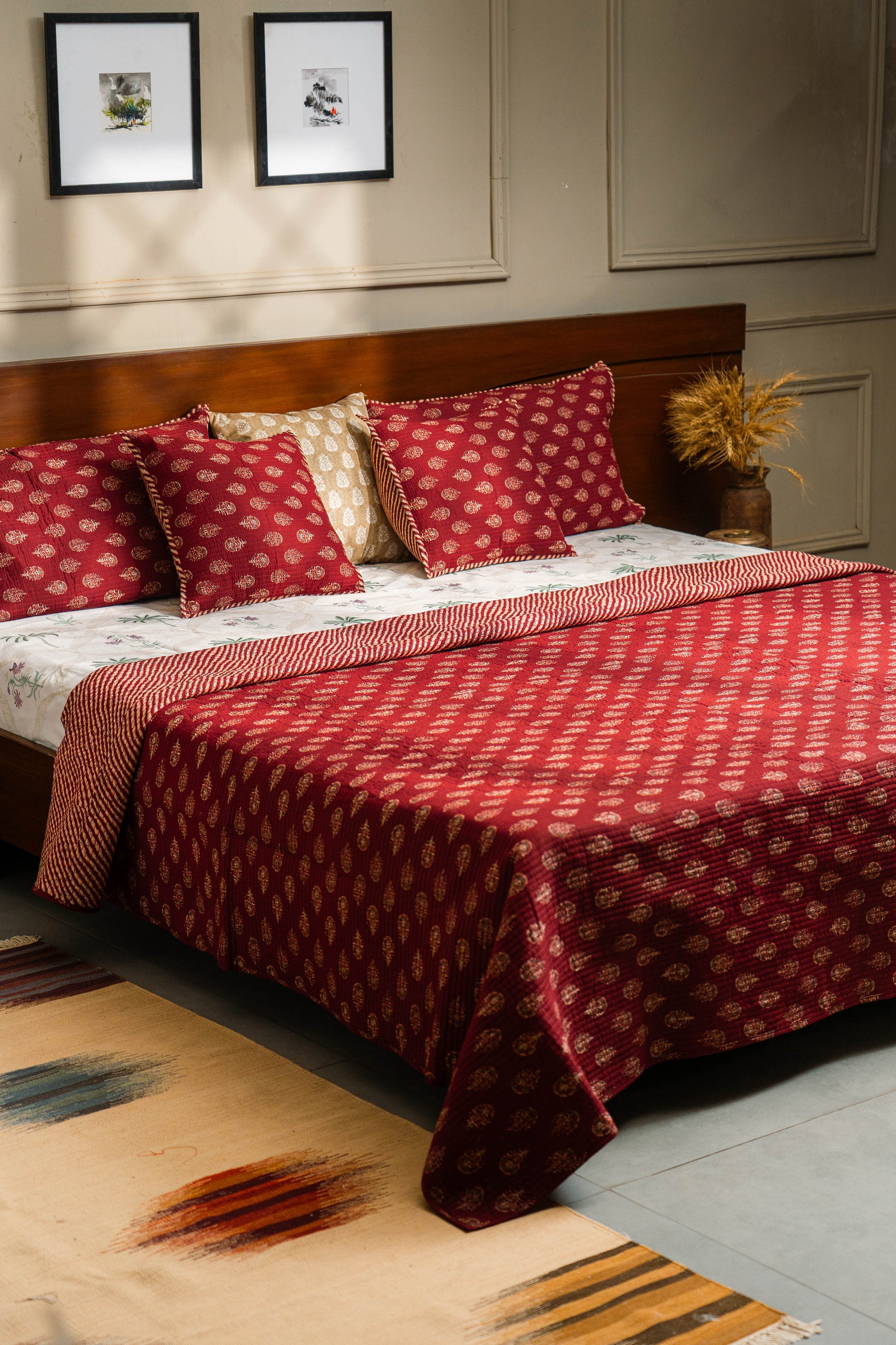 Bedroom with a bed covered in red and white patterned bedding, pillows, and a rug.
