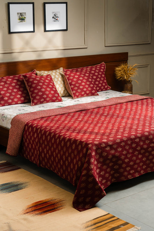 Bedroom with a bed covered in red and white patterned bedding, pillows, and a rug.