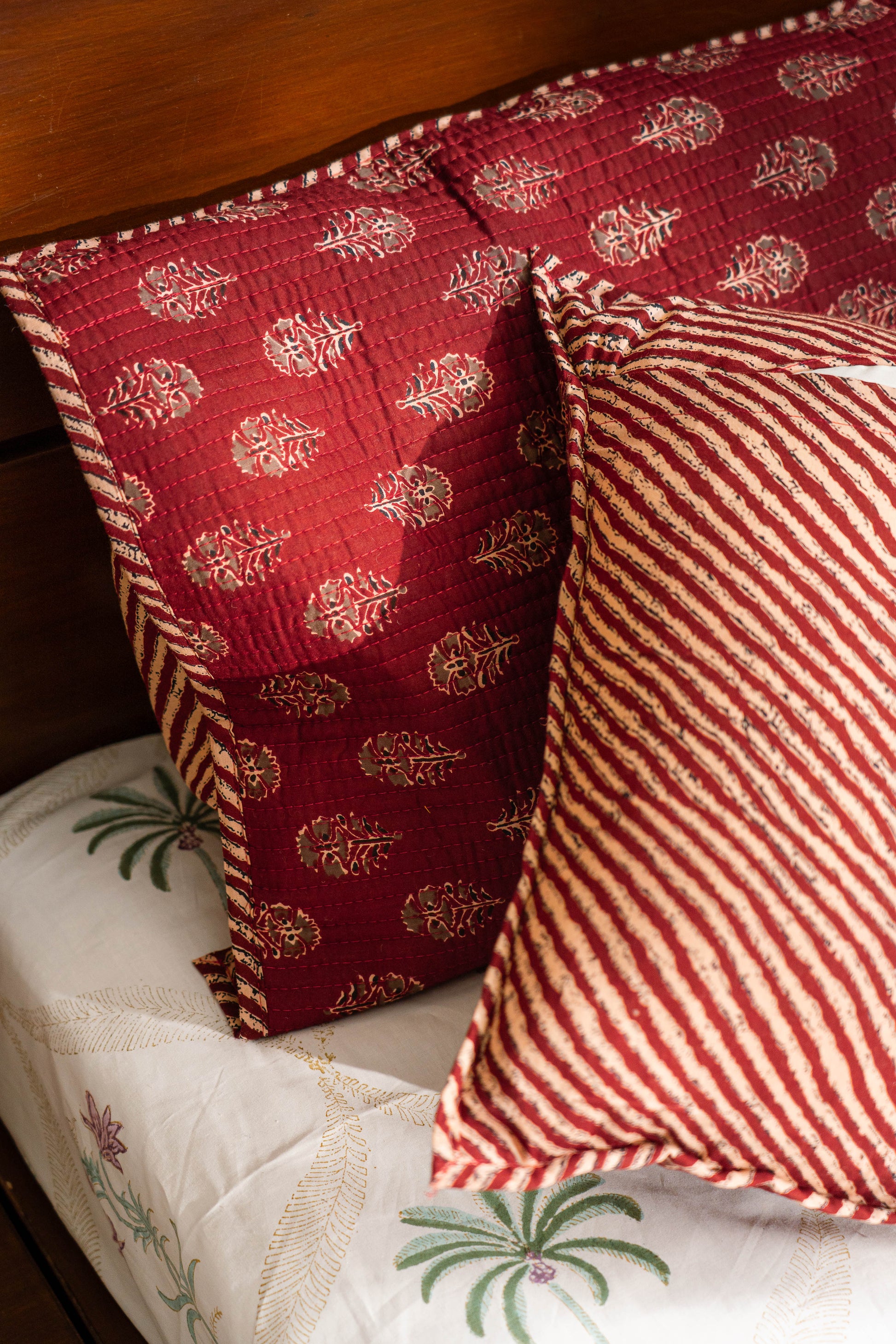 Red patterned pillow on a wooden surface with a striped pillow in the foreground.