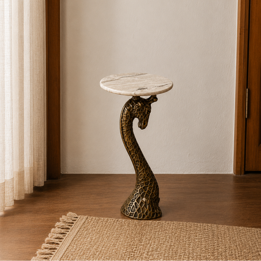 A decorative side table with a round white marble top and a sculpted bronze giraffe-head pedestal base, placed on a woven rug in a warm indoor setting.