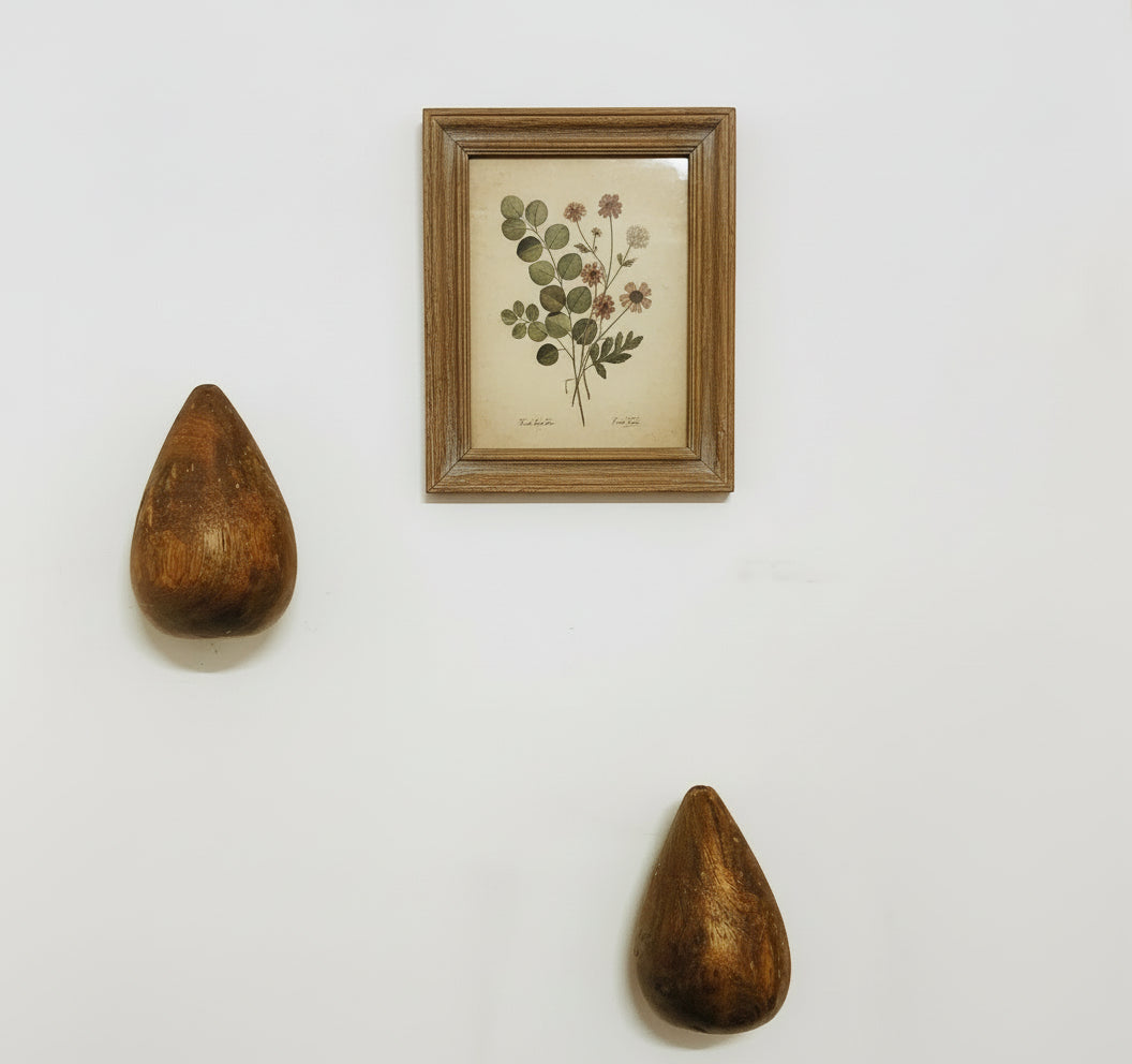 Two wooden sculptures and a framed botanical print on a white wall
