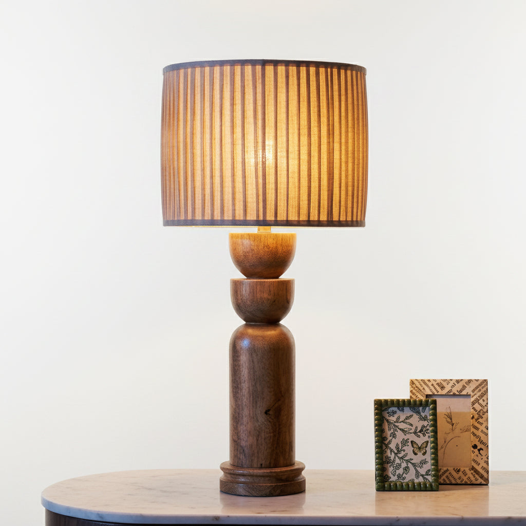 Wooden table lamp with pleated shade on a surface with decorative items.