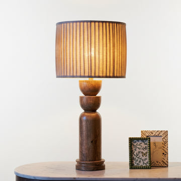 Wooden table lamp with pleated shade on a surface with decorative items.