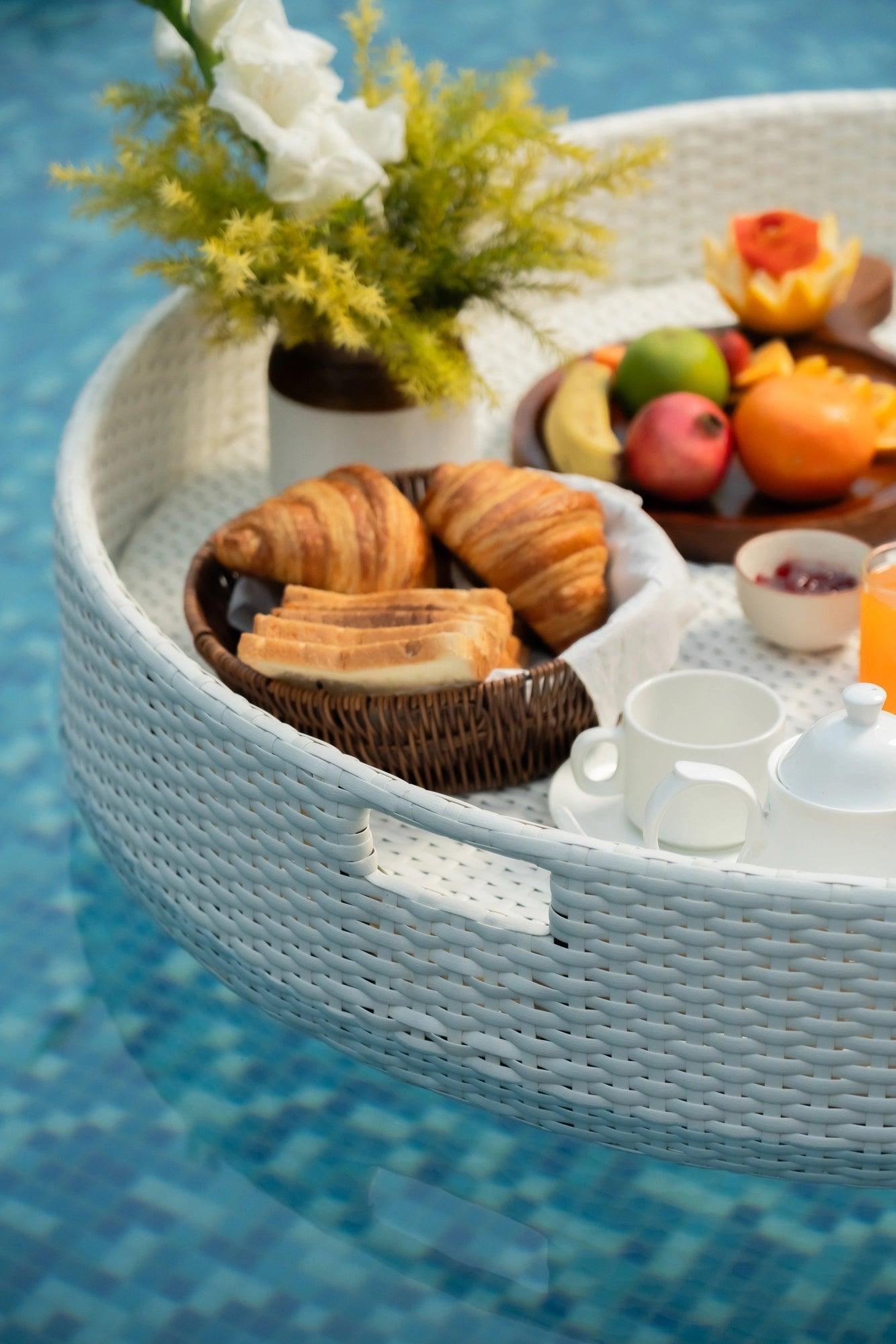 A white round floating serving tray filled with various food items and drinks, presented on a pool surface.