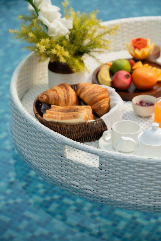 A white round floating serving tray filled with various food items and drinks, presented on a pool surface.