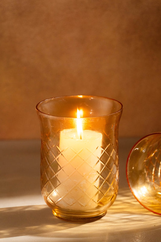 Candle in a textured glass holder on a warm-toned background