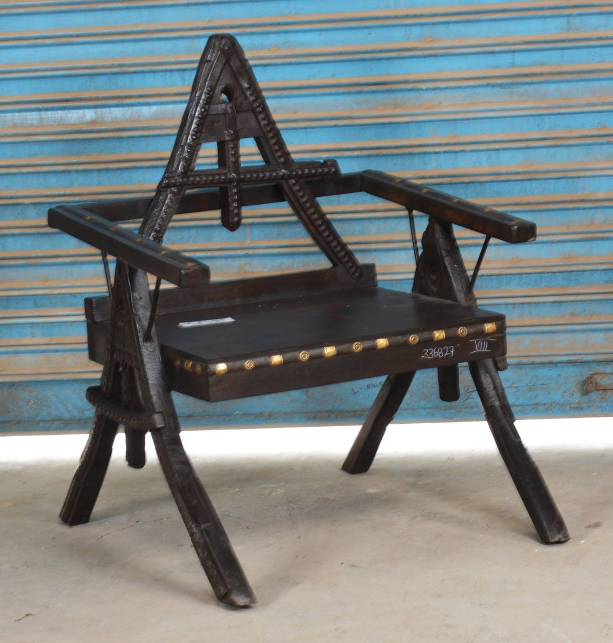 Made from solid teak wood, durable iron accents, and detailed brass stud work, this unique chair features a striking triangular backrest that sets it apart.
