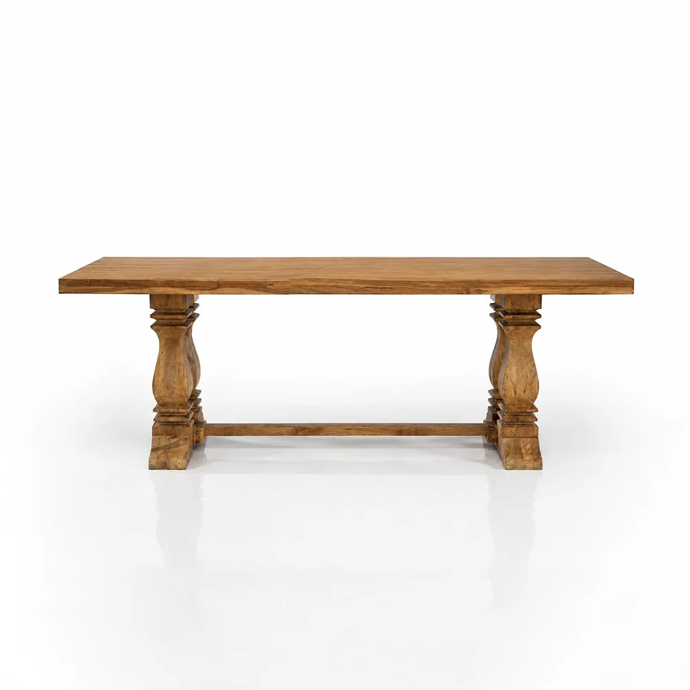 A rustic wooden dining table with a rectangular top and turned pedestal legs, shown on a clean white background with a soft reflection underneath.