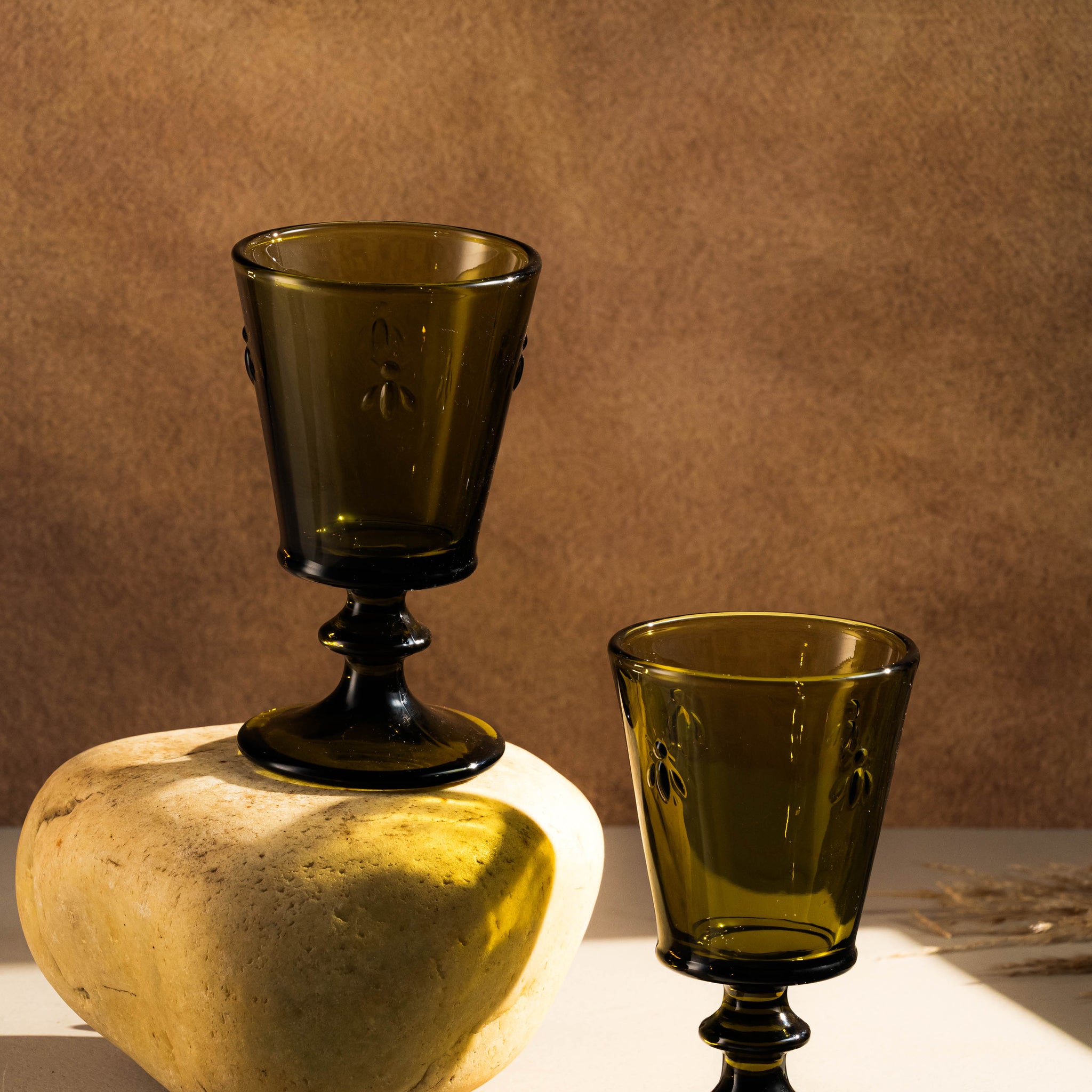 Two green glass goblets on a textured surface with a brown background