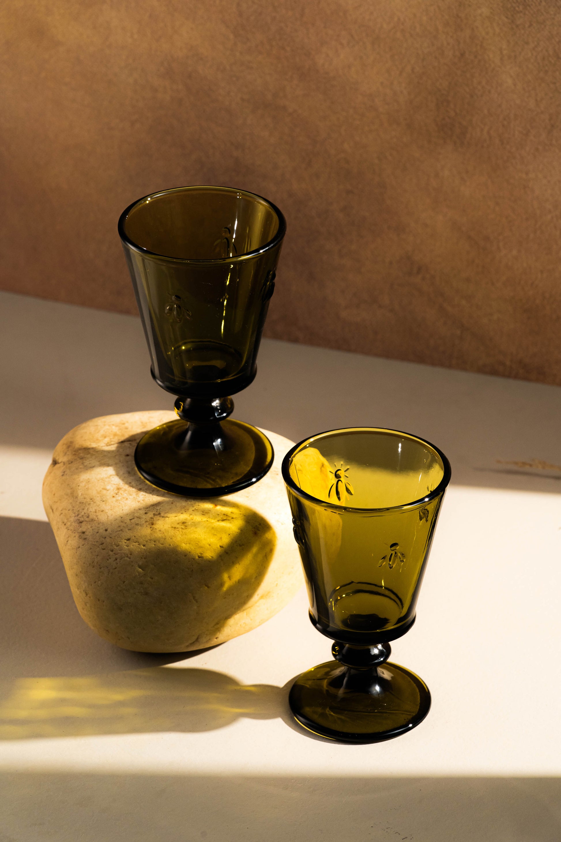 Two green glass goblets on a stone surface with a brown background