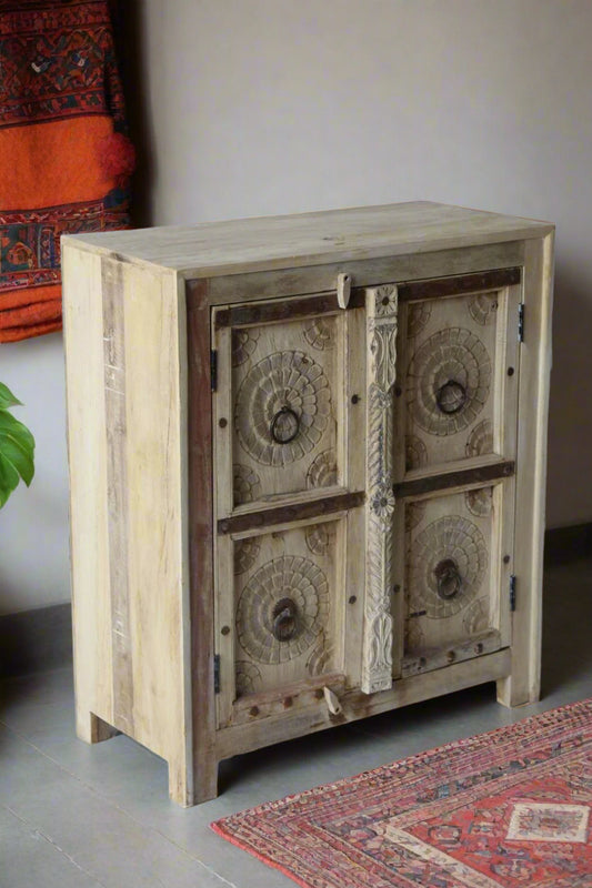 Wooden cabinet with decorative carvings against a stone wall.