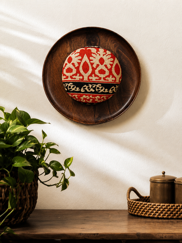 Decorative wooden plate with a red and white pattern on a white wall.