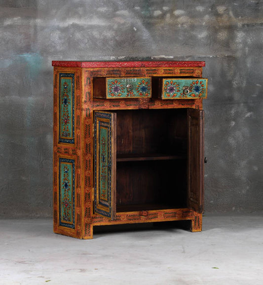 A hand-painted rustic wooden cabinet with a dark brown wood body, turquoise and red painted panels, and an open door showing an interior shelf, set against a textured gray wall.