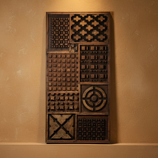 A tall rectangular wooden decorative panel with multiple carved geometric and textured square panels, photographed against a plain gray wall and light floor.