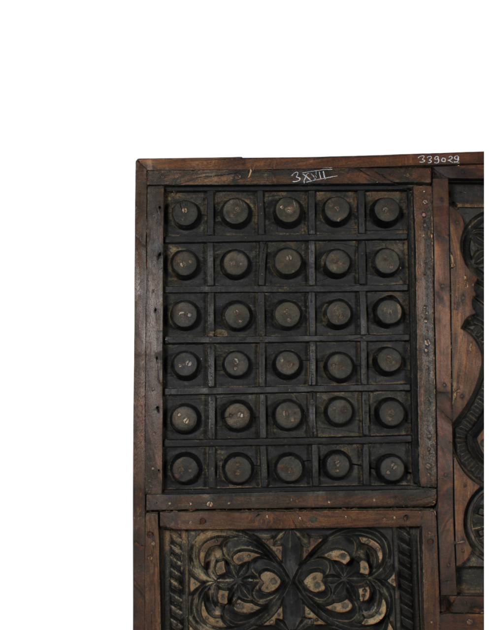 A close-up of a dark carved wooden cabinet or storage panel with a grid of round metal knobs and ornate floral carvings, shown against a plain white background.