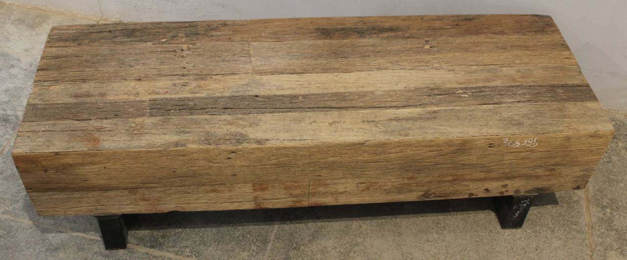 A rustic rectangular wooden bench or coffee table made from weathered reclaimed wood planks, supported by a black metal frame, shown against a neutral concrete background.