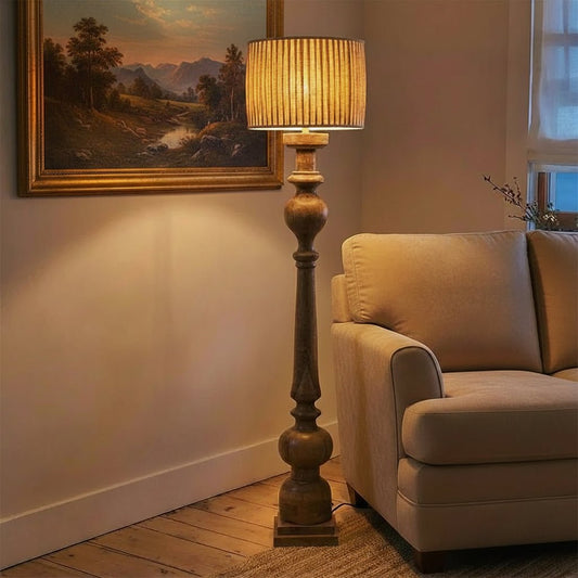 Floor lamp with a beige shade next to a gray armchair in a room with wooden flooring.