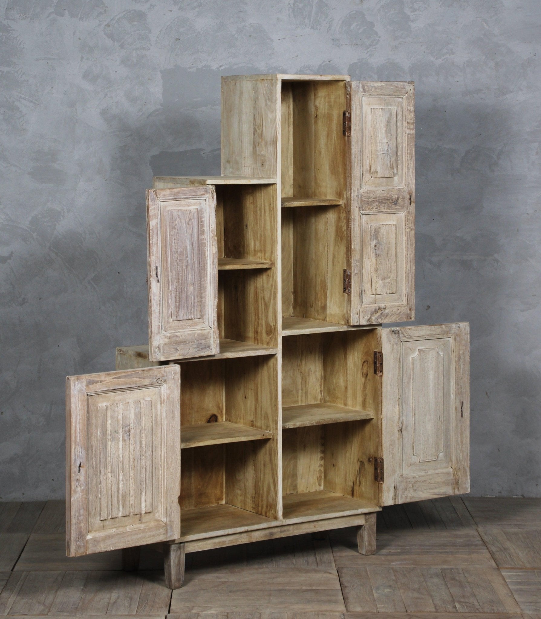 Stack of wooden shelves with open doors against a gray wall.