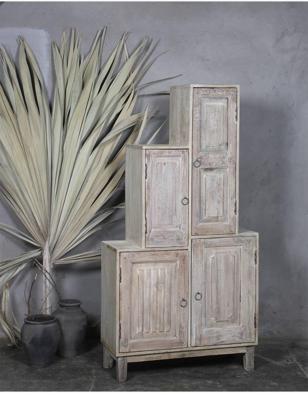 Stack of rustic wooden cabinets against a gray wall with plants.