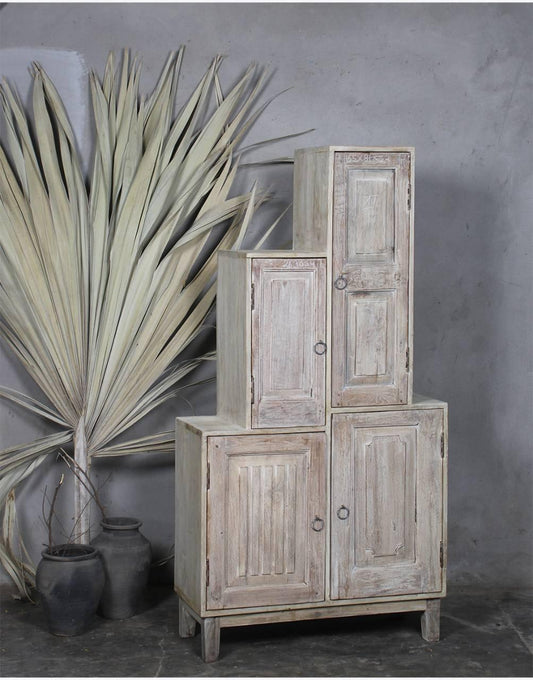 Stack of rustic wooden cabinets against a gray wall with plants.