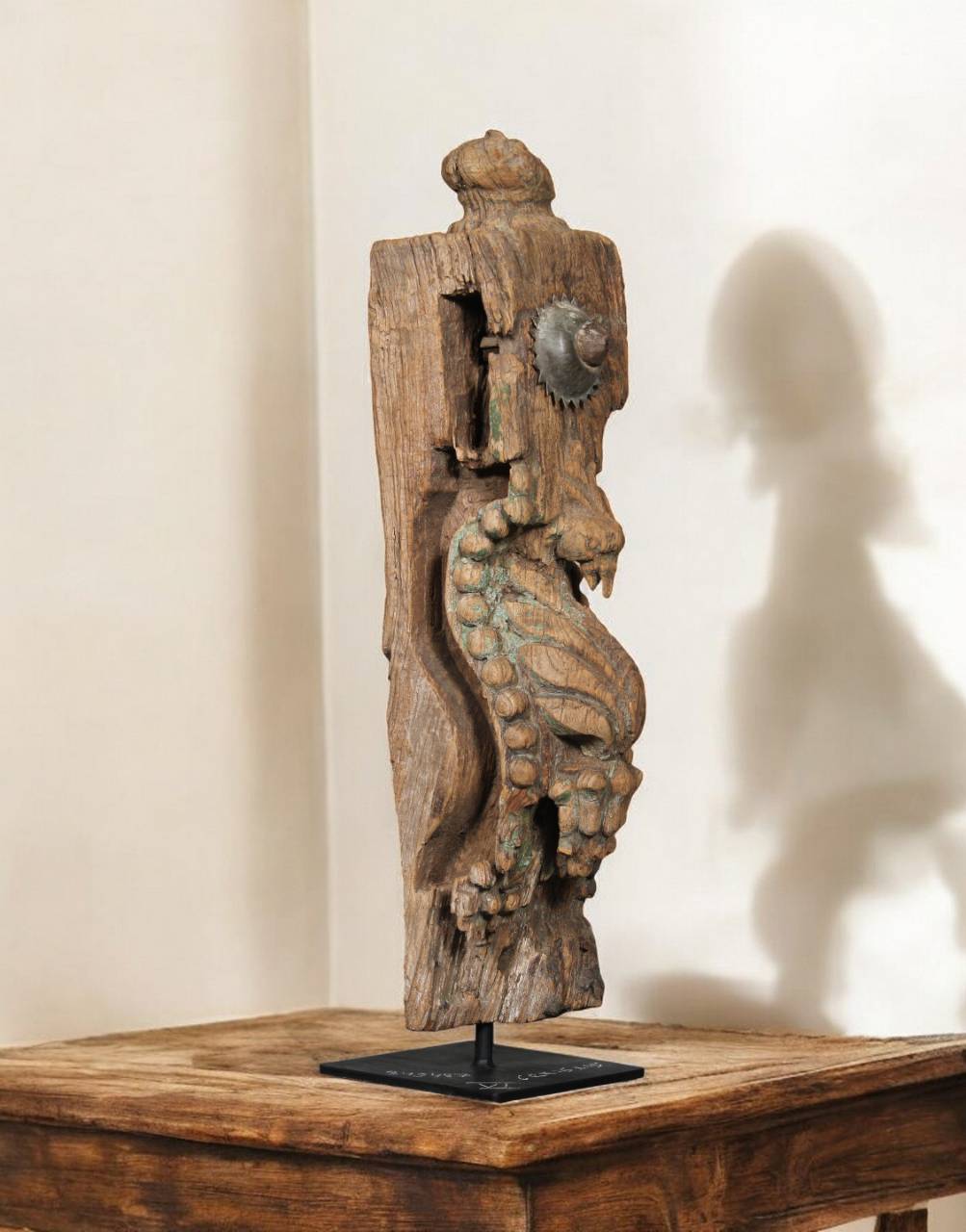Wooden sculpture of a seahorse on a stand against a beige wall