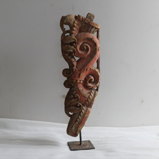 Wooden mask with intricate carvings on a stand against a plain background
