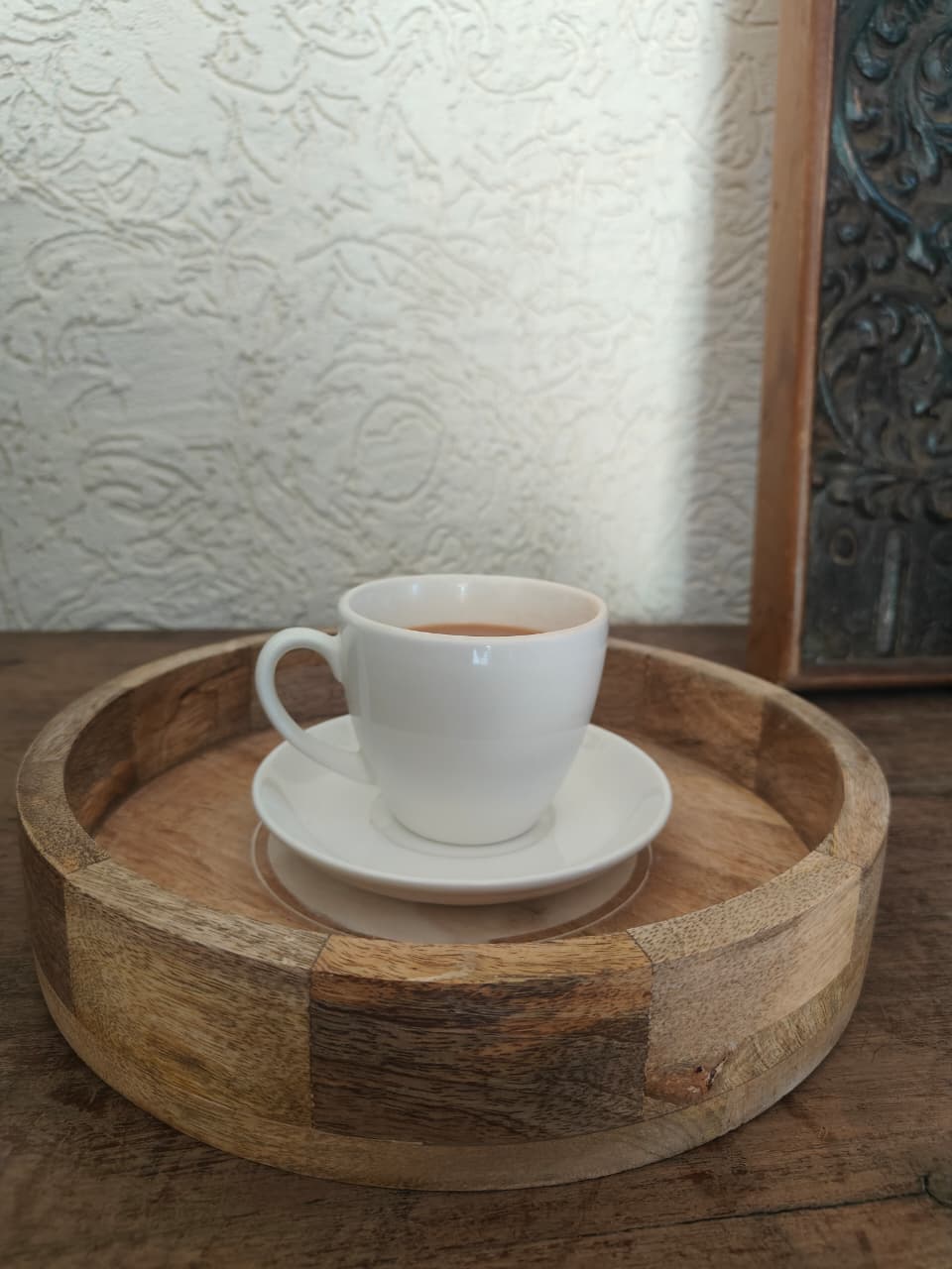 White cup and saucer on a wooden tray with a textured wall in the background