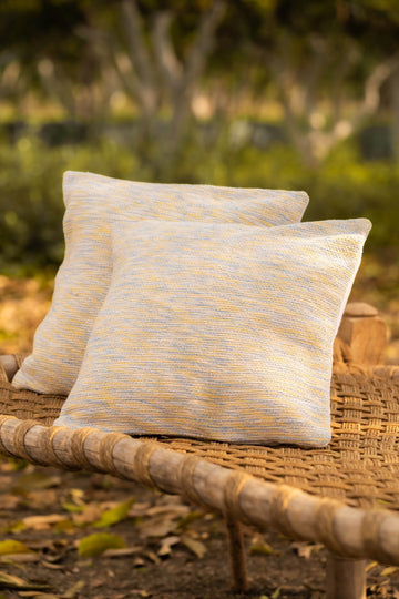 Two patterned pillows on a wicker chair with a blurred natural background