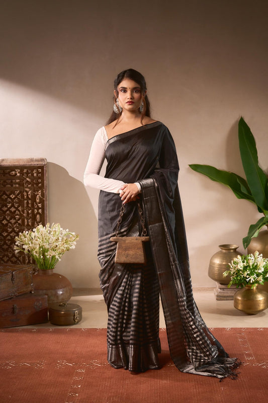 Woman in a black saree with a white blouse standing in a decorated room.