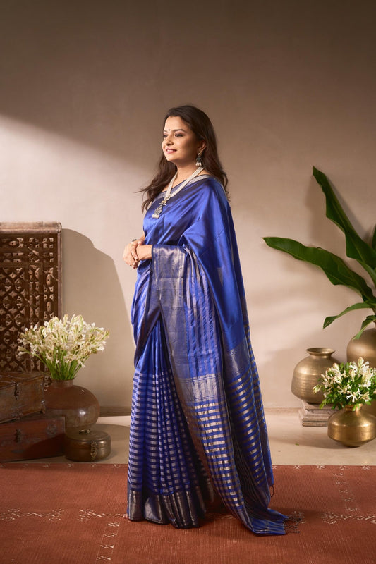 Woman in a blue saree standing in a room with decorative elements.