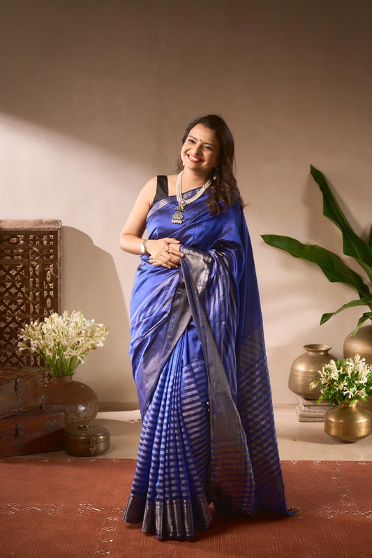 Woman in a blue saree standing in a room with decorative elements.