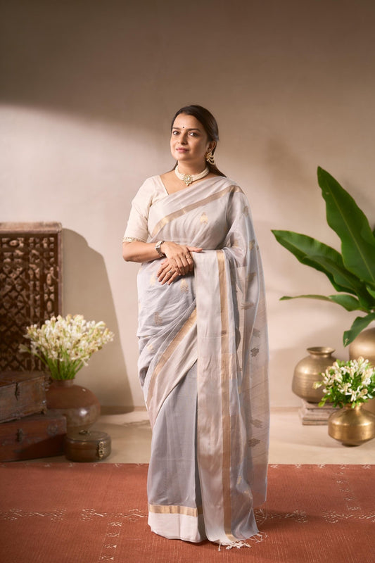 Woman in a white saree standing in a room with decorative elements.