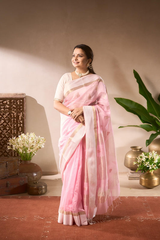 Woman in a pink saree standing in a room with decorative elements.