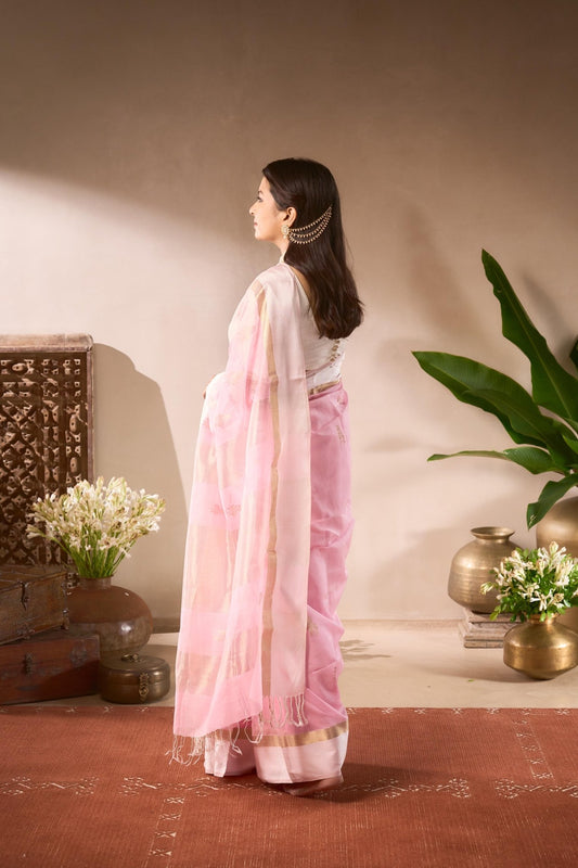 Woman in a pink saree standing in a room with decorative elements.