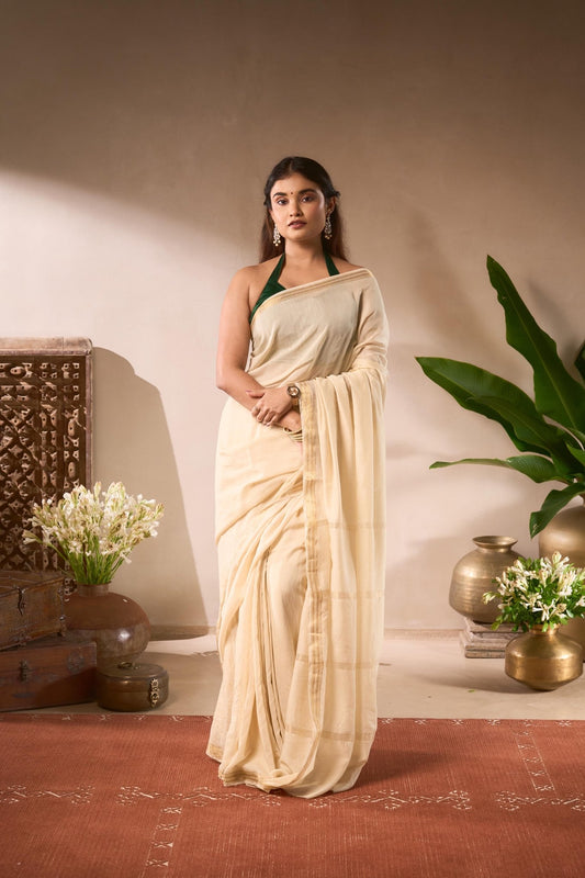 Woman in a beige saree standing in a decorated room with plants and decorative items.
