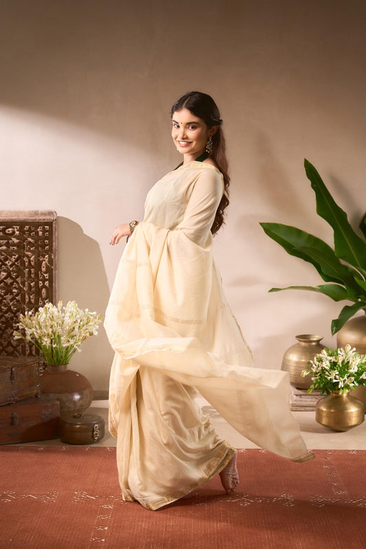 Woman in a white saree standing in a room with decorative elements.