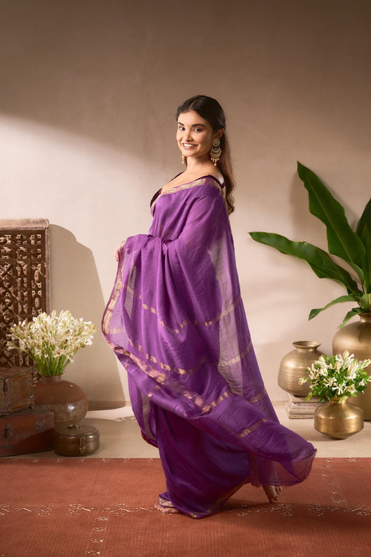 Woman in a purple saree standing in a room with decorative elements.