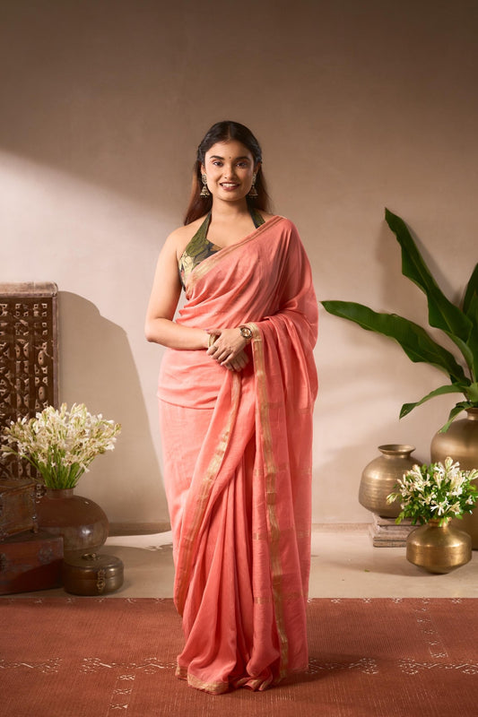 Woman in a pink saree standing in a decorated room with plants and vases.