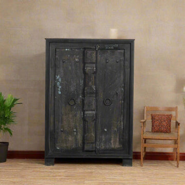 Vintage-style black cabinet with wooden chair and plant against a beige wall.