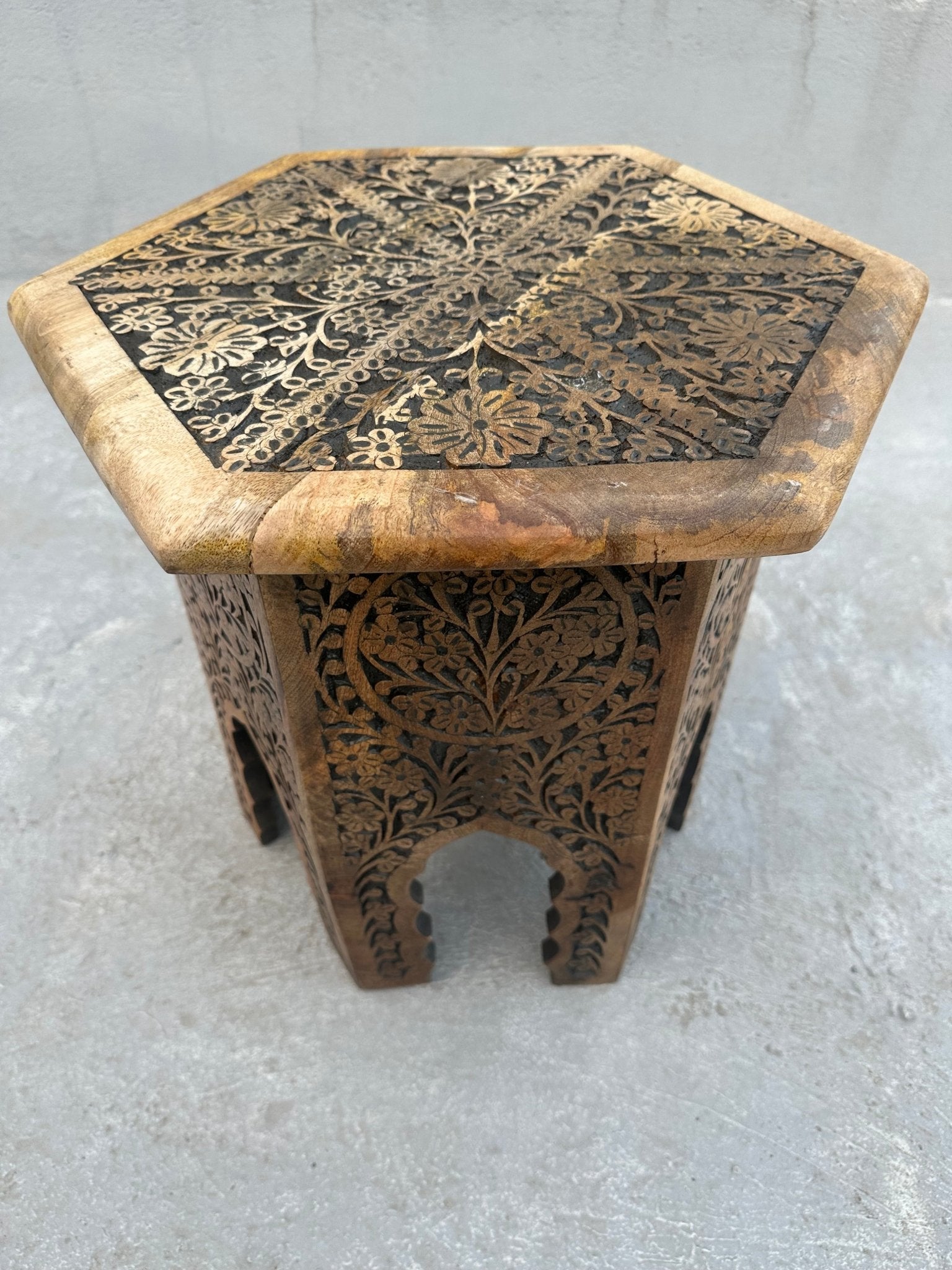 Hexagonal wooden side table with intricate carvings on a gray surface