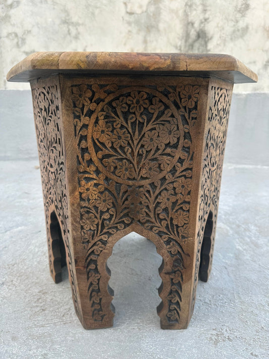 Wooden side table with intricate carvings on a light gray background