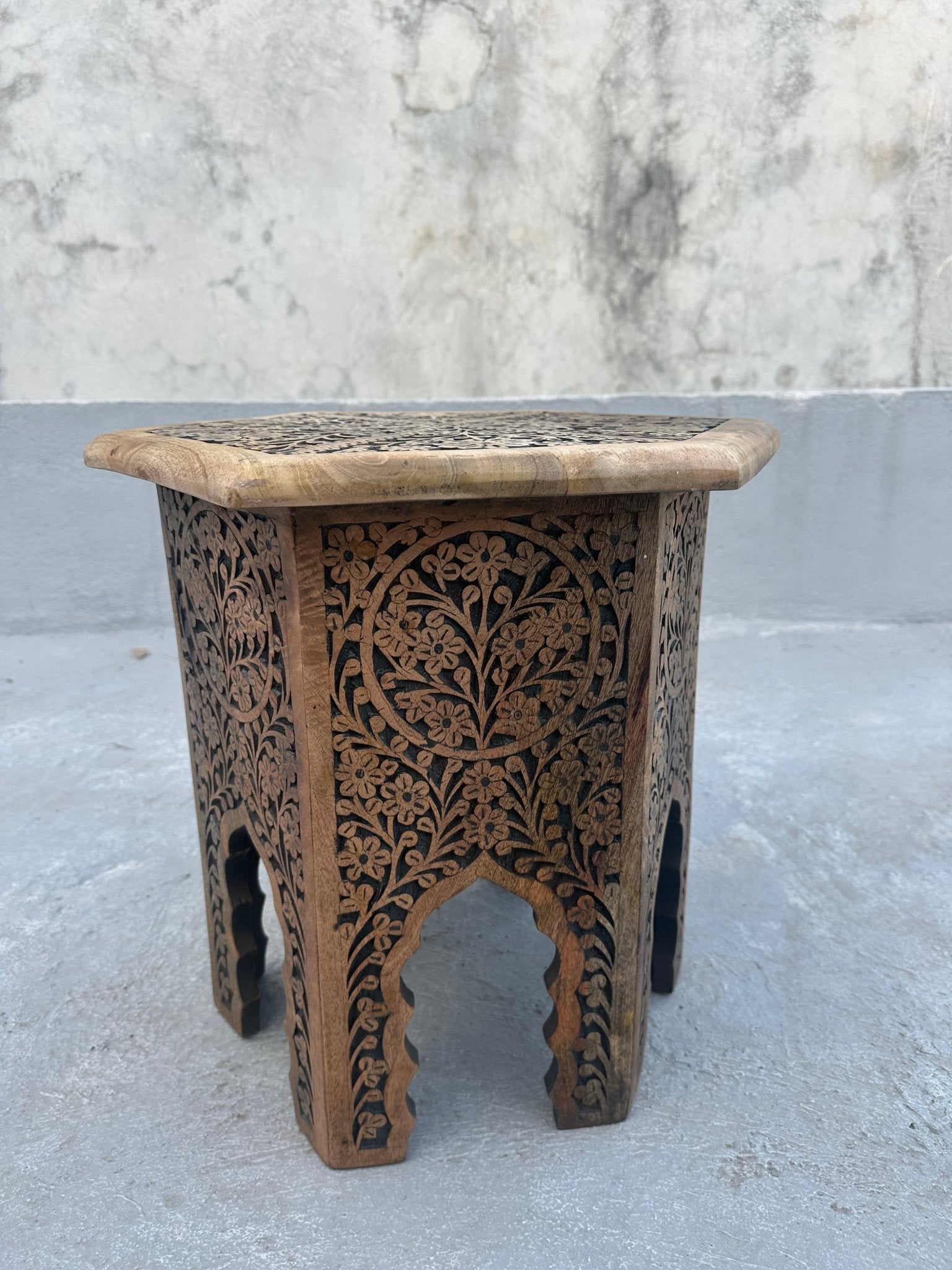 Wooden side table with intricate carvings on a concrete surface